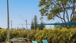 A swimming pool with lounge chairs, surrounded by tropical plants and a stone wall. - The Carmel Yamba (Yamba)