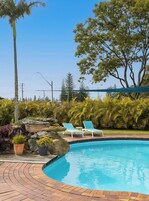 A swimming pool with lounge chairs, surrounded by tropical plants and a stone wall.