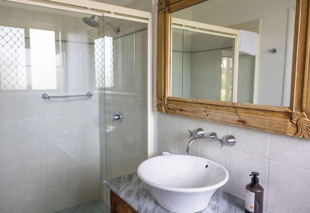 Une salle de bain dotée d’une douche à parois de verre, d’un lavabo blanc, d’un miroir à cadre en bois et d’un plan de toilette en marbre.