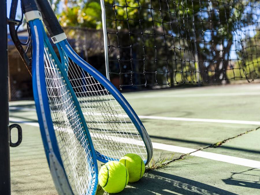 En tennisbane med net, en blå tennisraket og to tennisbolde.