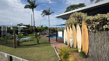 Zona exterior tancada amb piscina, palmeres i uns surfboards adossats a una paret.