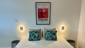 A neatly made bed with two pillows, a framed movie poster above, and two wall-mounted lights on either side. - The Carmel Yamba (Yamba)