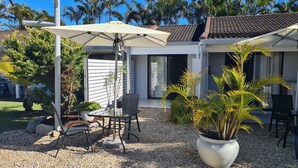 A covered patio area with a table and chairs, surrounded by potted plants and a gravel ground. - The Carmel Yamba (Yamba)