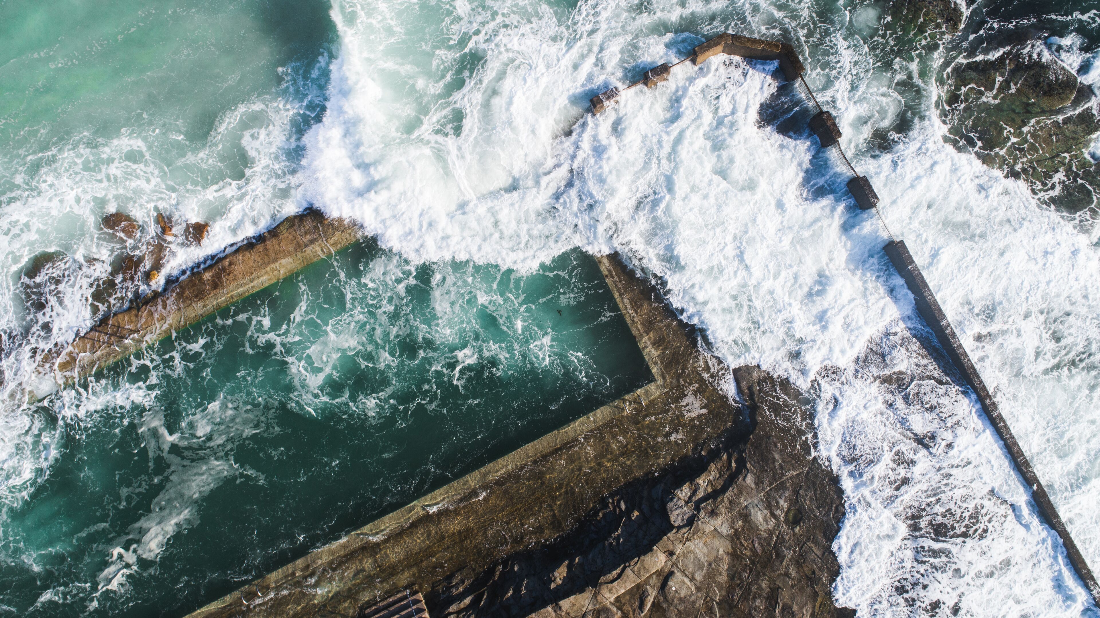 Vista aérea de una zona costera con formaciones rocosas y olas rompiendo contra ellas.