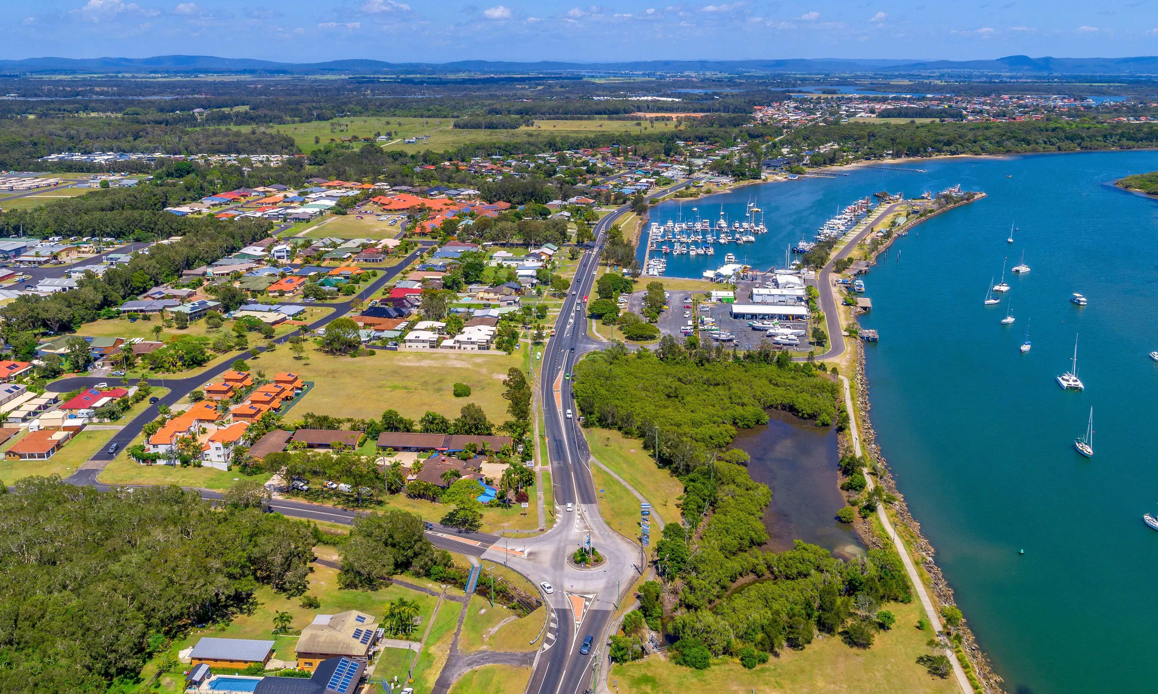 An aerial view of a coastal town with residential areas, roads, and a marina with boats.