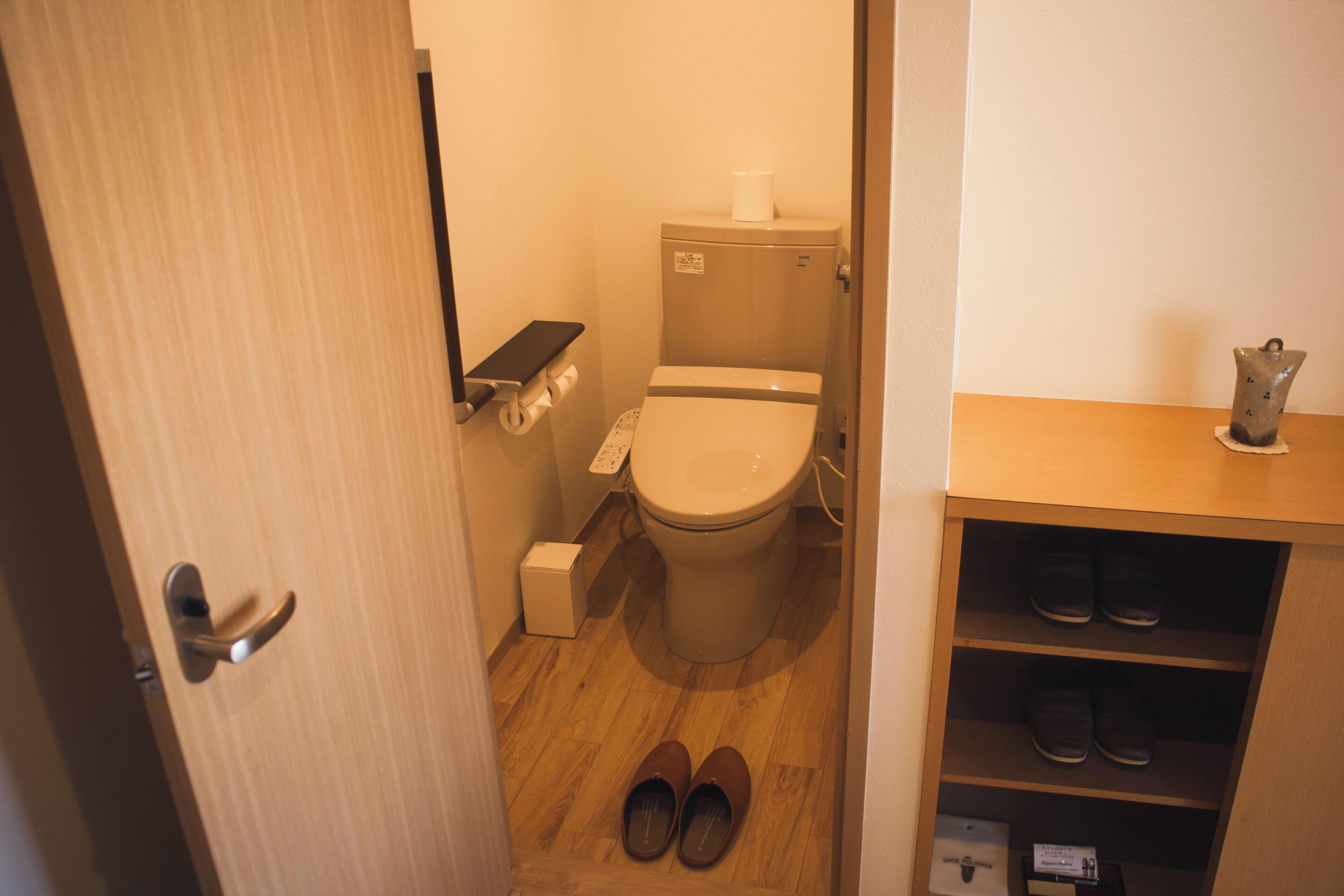 A small bathroom with a toilet, a shelf with shoes, and a door.