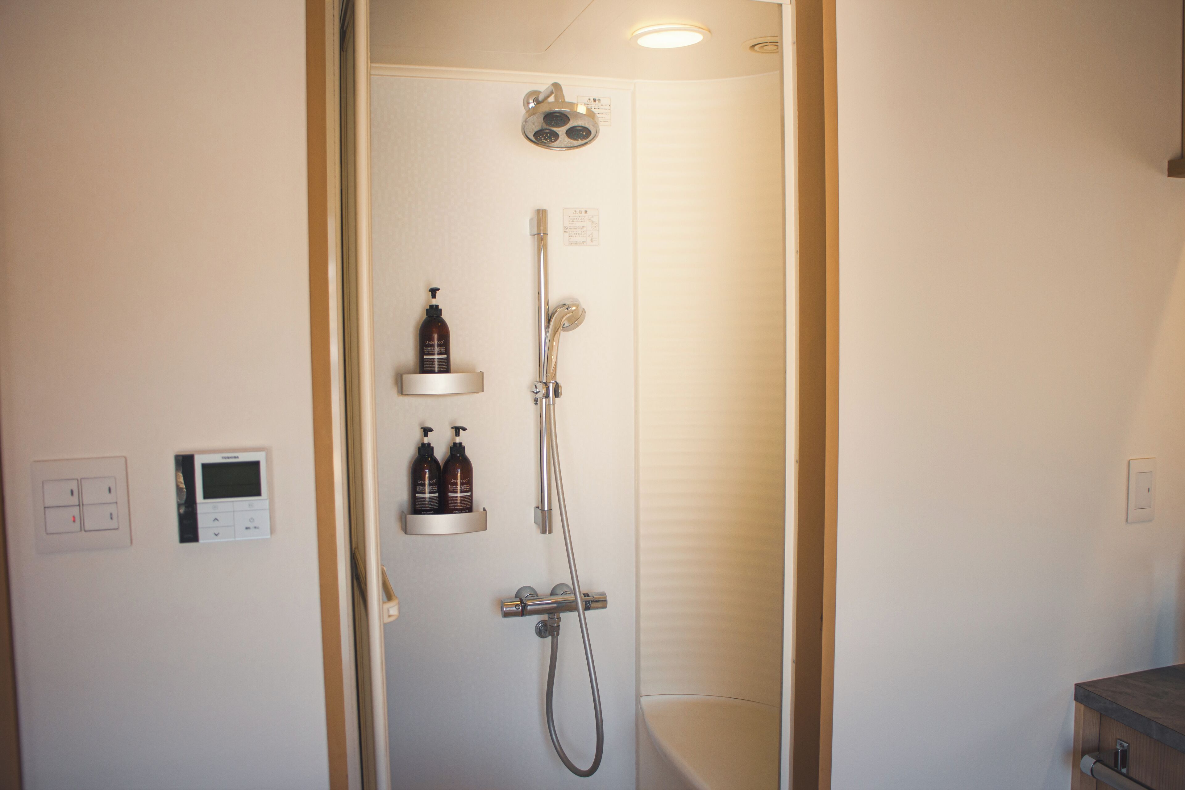 Un baño moderno con ducha, inodoro y lavabo. Hay dos botellas de champú en una repisa.