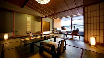 A traditional Japanese room with tatami flooring, a low table, and a view of a cityscape through large windows.