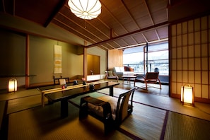 A traditional Japanese room with tatami flooring, a low table, and a view of a cityscape through large windows. - Aburaya Tosen (Yamanouchi)