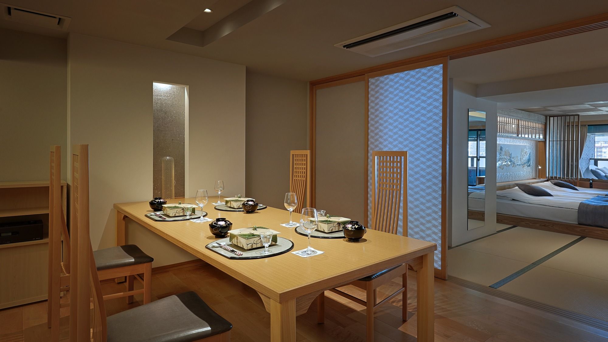 A traditional Japanese-style room with tatami flooring, a low table set for dining, and sliding doors leading to a bed.