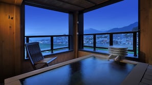 A room with a view of a cityscape and mountains, a wooden chair, and a stone hot tub. - Aburaya Tosen (Yamanouchi)