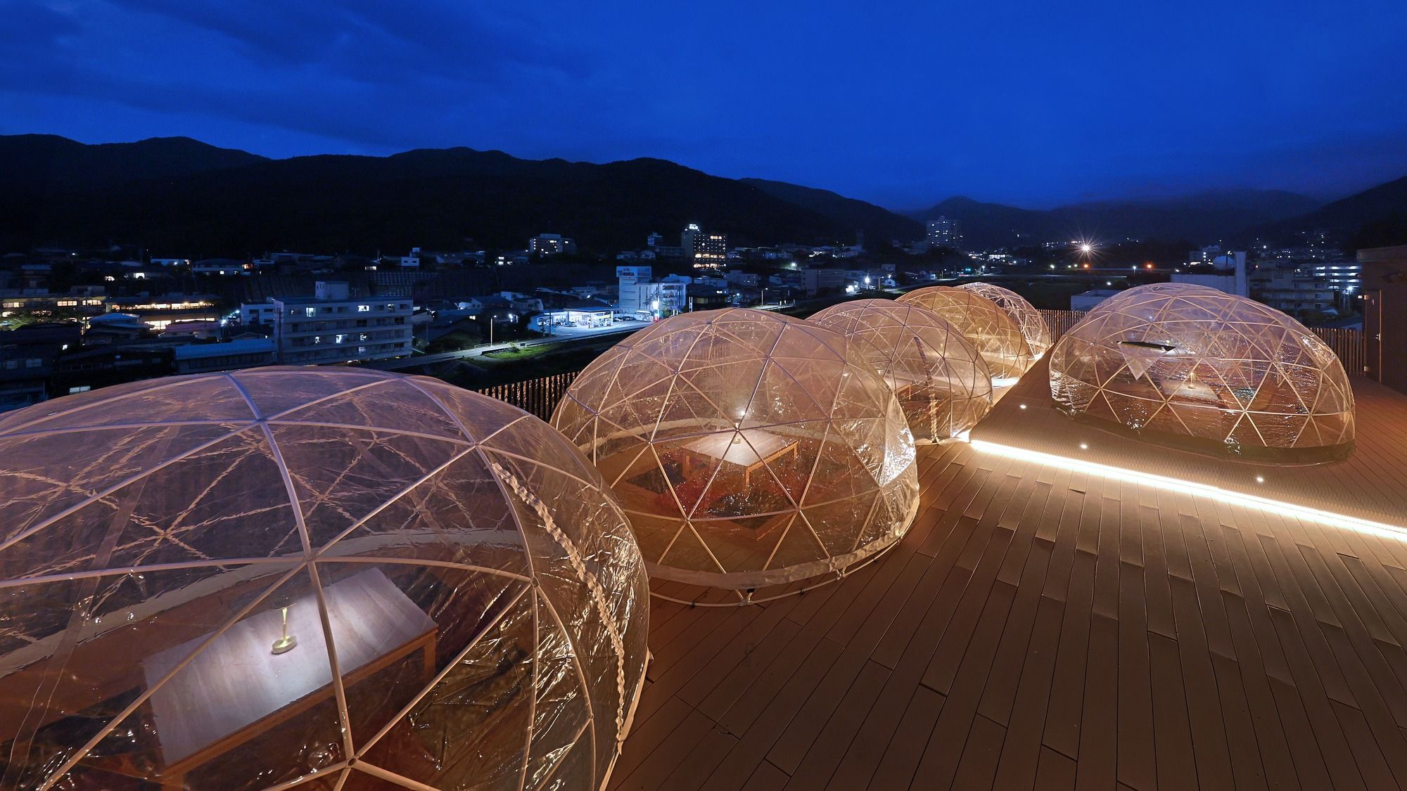 Transparent geodesic domes on a wooden deck with a cityscape in the background.