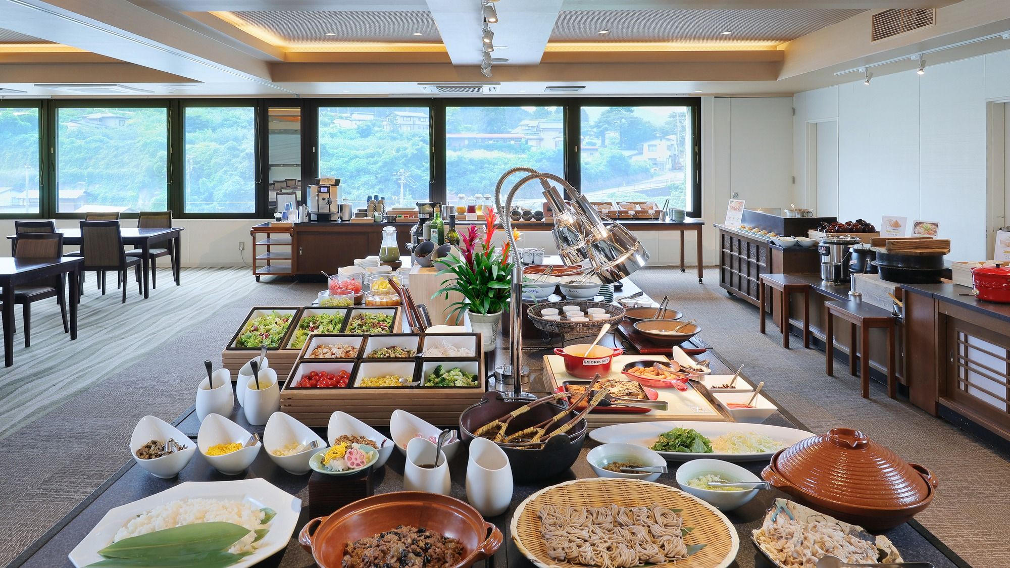 A buffet setup with various food items and a view of the outdoors through large windows.