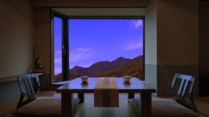 A dining area with a table and chairs, a view of mountains, and a door leading outside. - Aburaya Tosen (Yamanouchi)