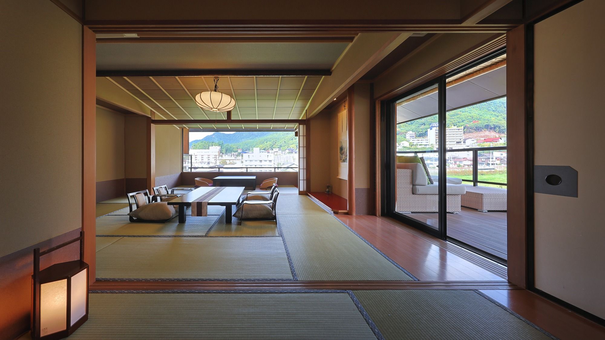 A traditional Japanese room with tatami flooring, a low table, cushions, and a view of a cityscape through large windows.
