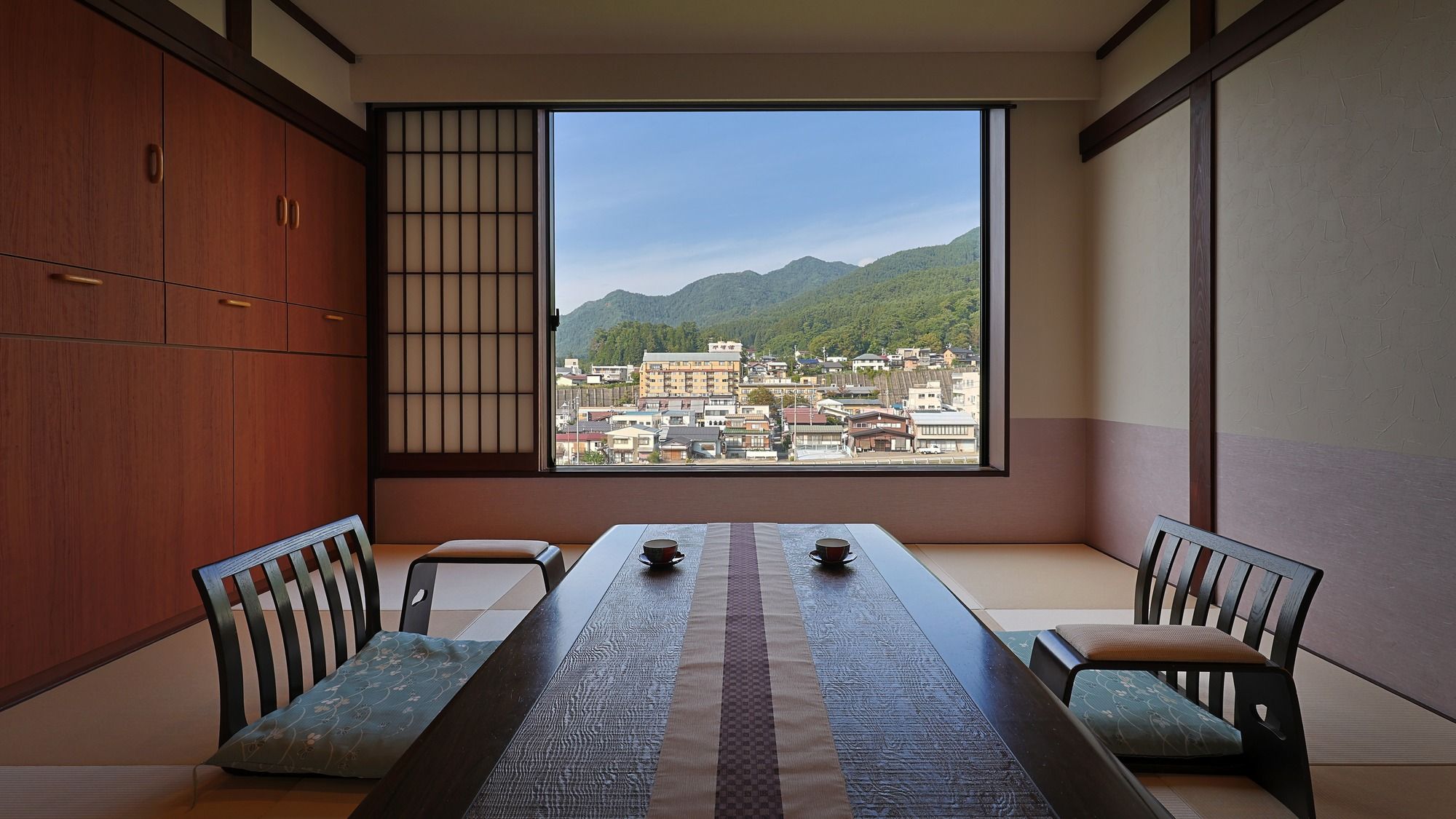Ein traditioneller japanischer Raum mit Tatami-Böden, einem niedrigen Tisch mit zwei Tassen und Blick auf eine Stadtlandschaft durch ein großes Fenster.