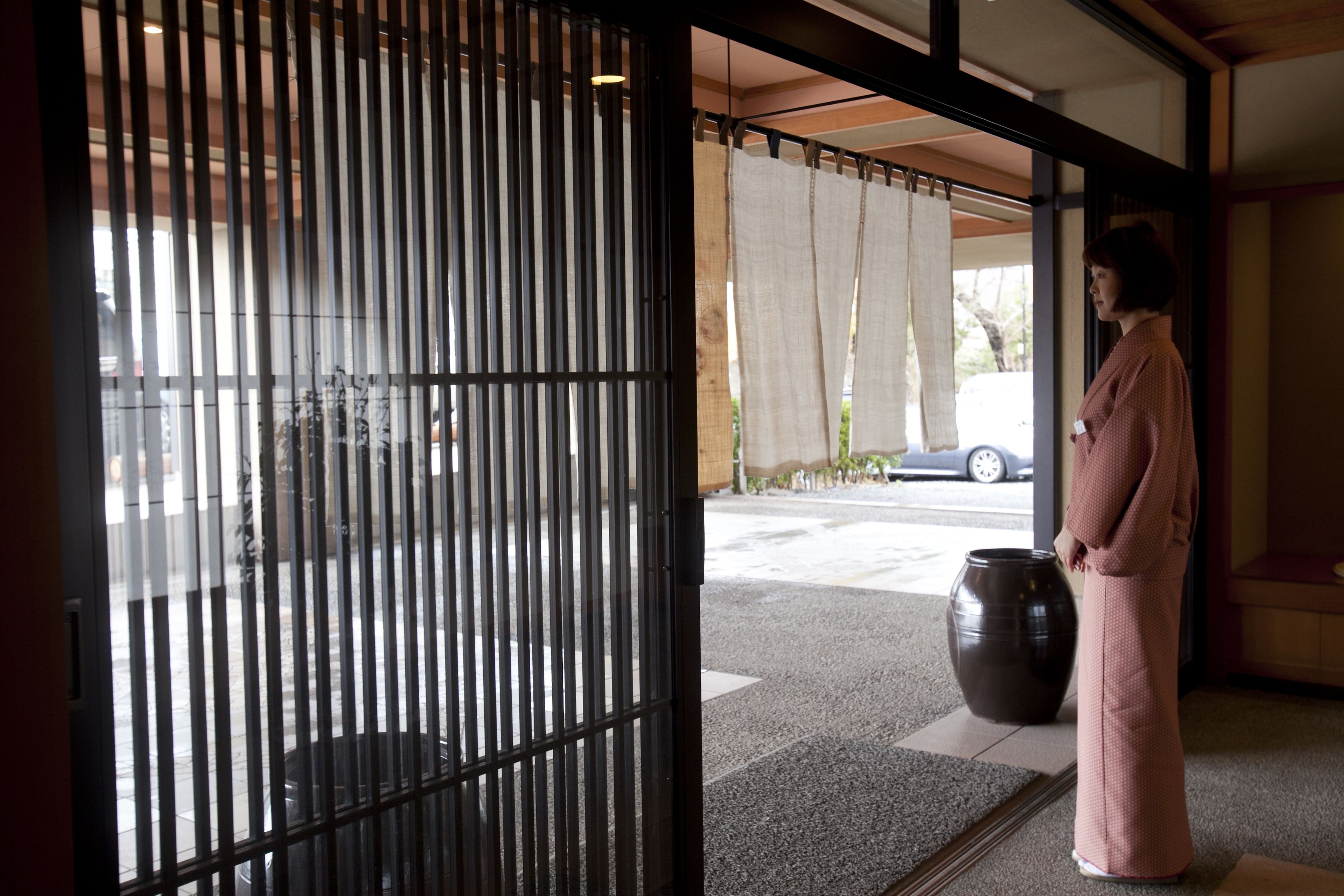 Un interior japonés tradicional con un fusuma, un gran jarrón de cerámica y una persona de pie junto a la puerta.
