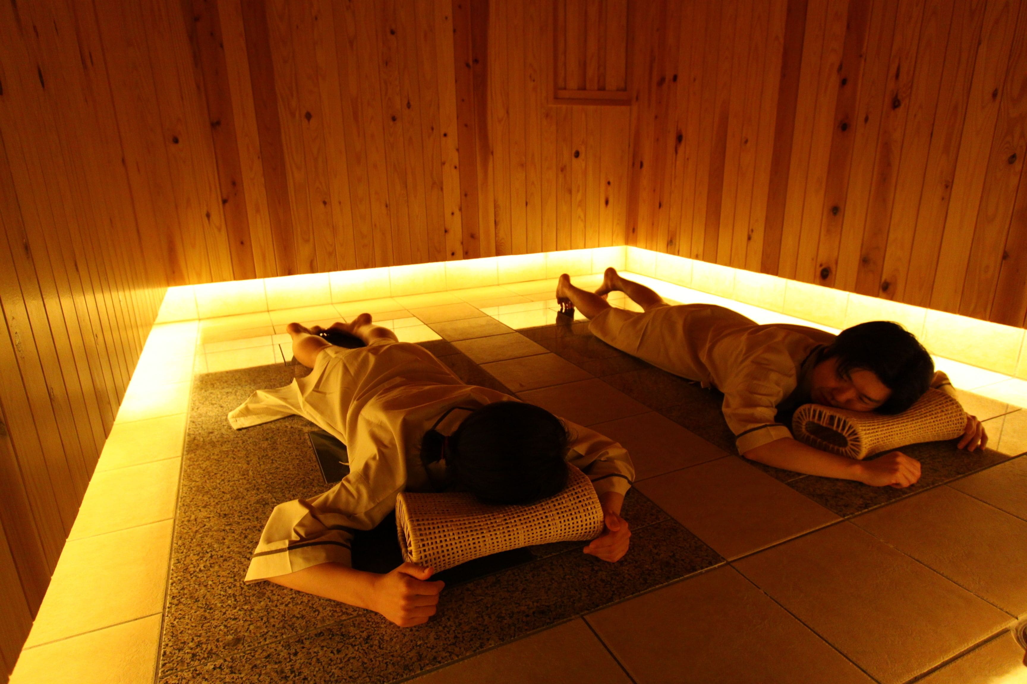 Two people lying on mats in a wooden room with a low ceiling.