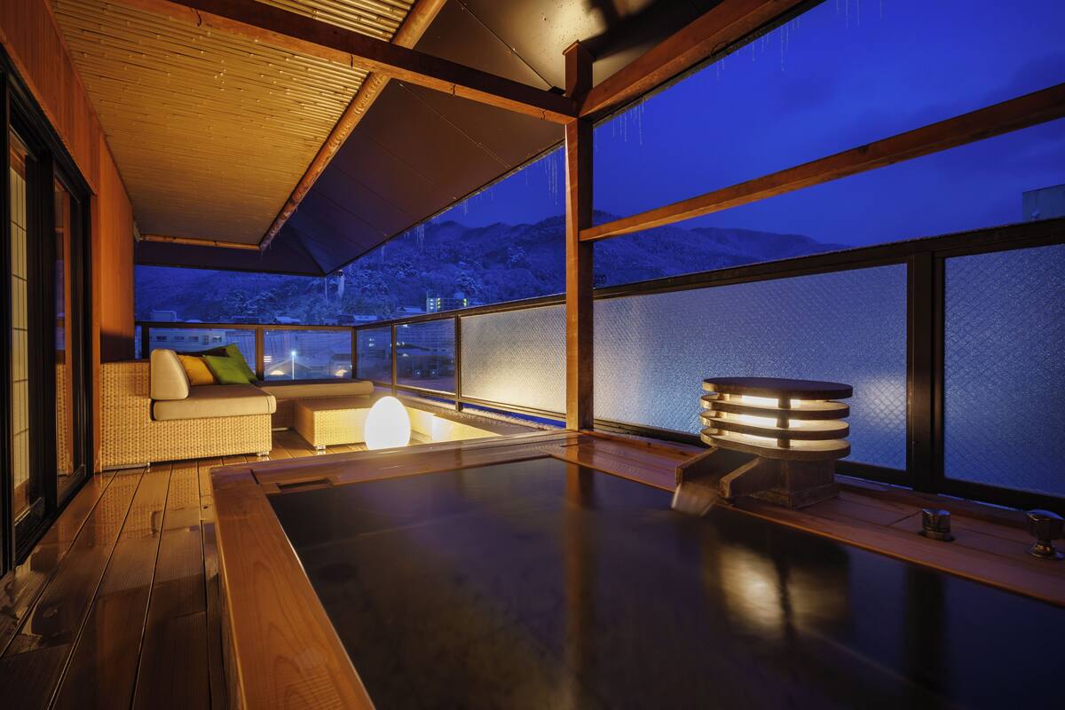 Un intérieur moderne avec un plancher en bois, un canapé avec des coussins, une petite table et une grande fenêtre donnant sur des montagnes enneigées.