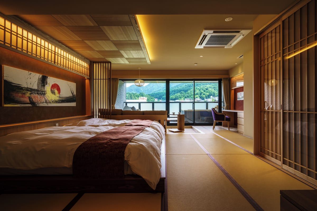Une chambre de style japonais traditionnel, avec un sol recouvert de tatamis, un grand lit, une porte coulissante et une vue sur la verdure.