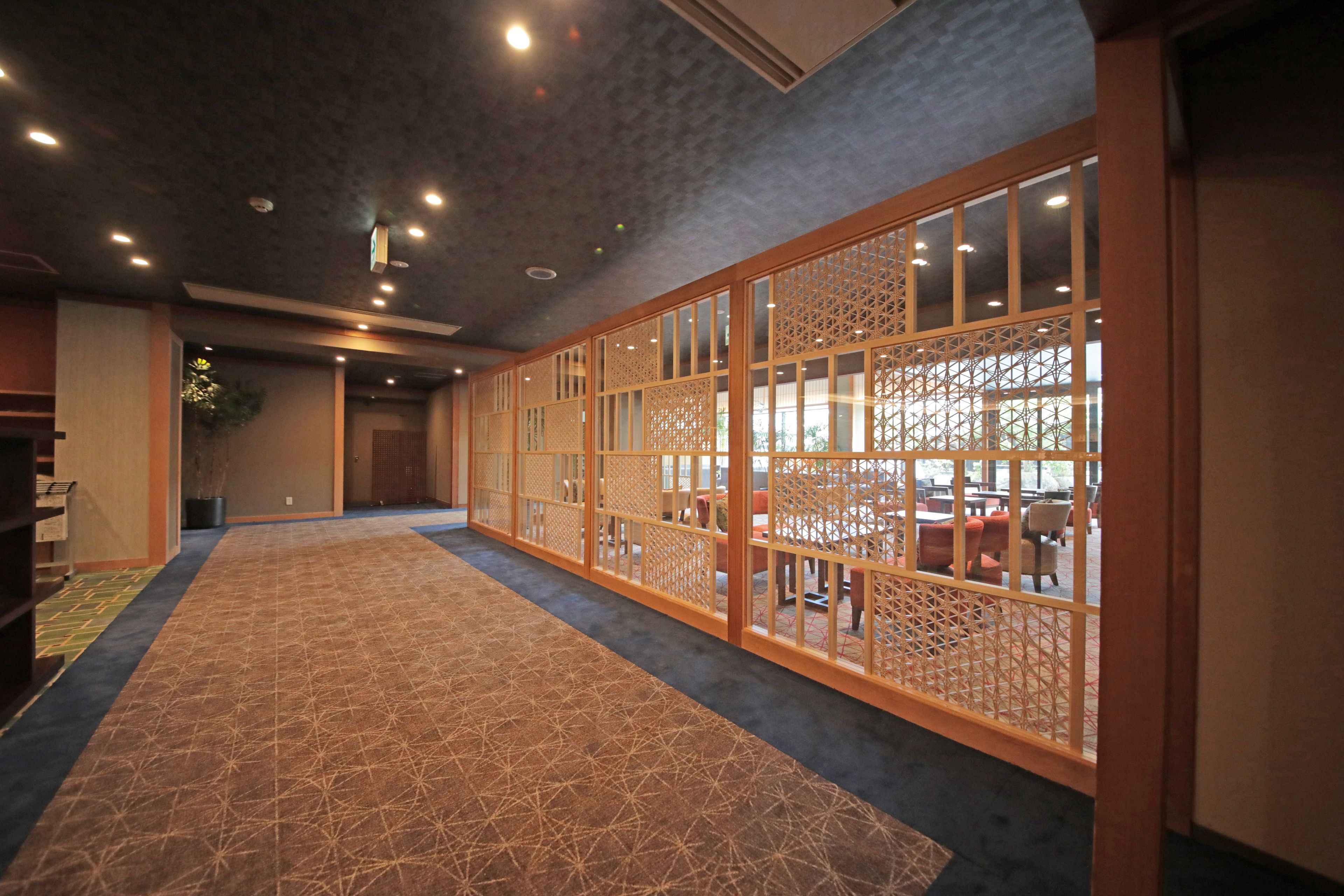 A hallway with a patterned carpet, wooden sliding doors with lattice designs, and recessed ceiling lights.