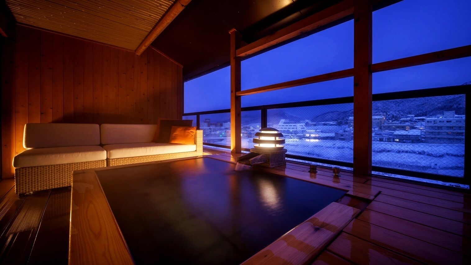 A wooden interior with a sofa and a view of a snowy landscape through large windows.