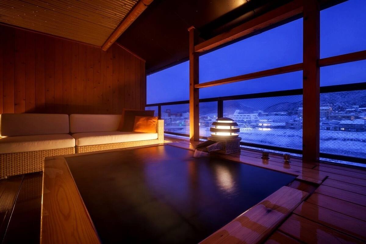 Un intérieur en bois avec un canapé et une vue sur un paysage enneigé, visible à travers de grandes fenêtres.
