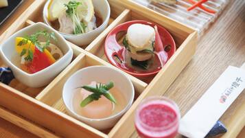 A wooden tray with various food items including a bowl of soup, a bowl of salad, a dish with a fish sandwich, and a glass of pink drink.
