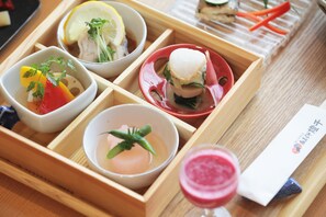 A wooden tray with various food items including a bowl of soup, a bowl of salad, a dish with a fish sandwich, and a glass of pink drink.