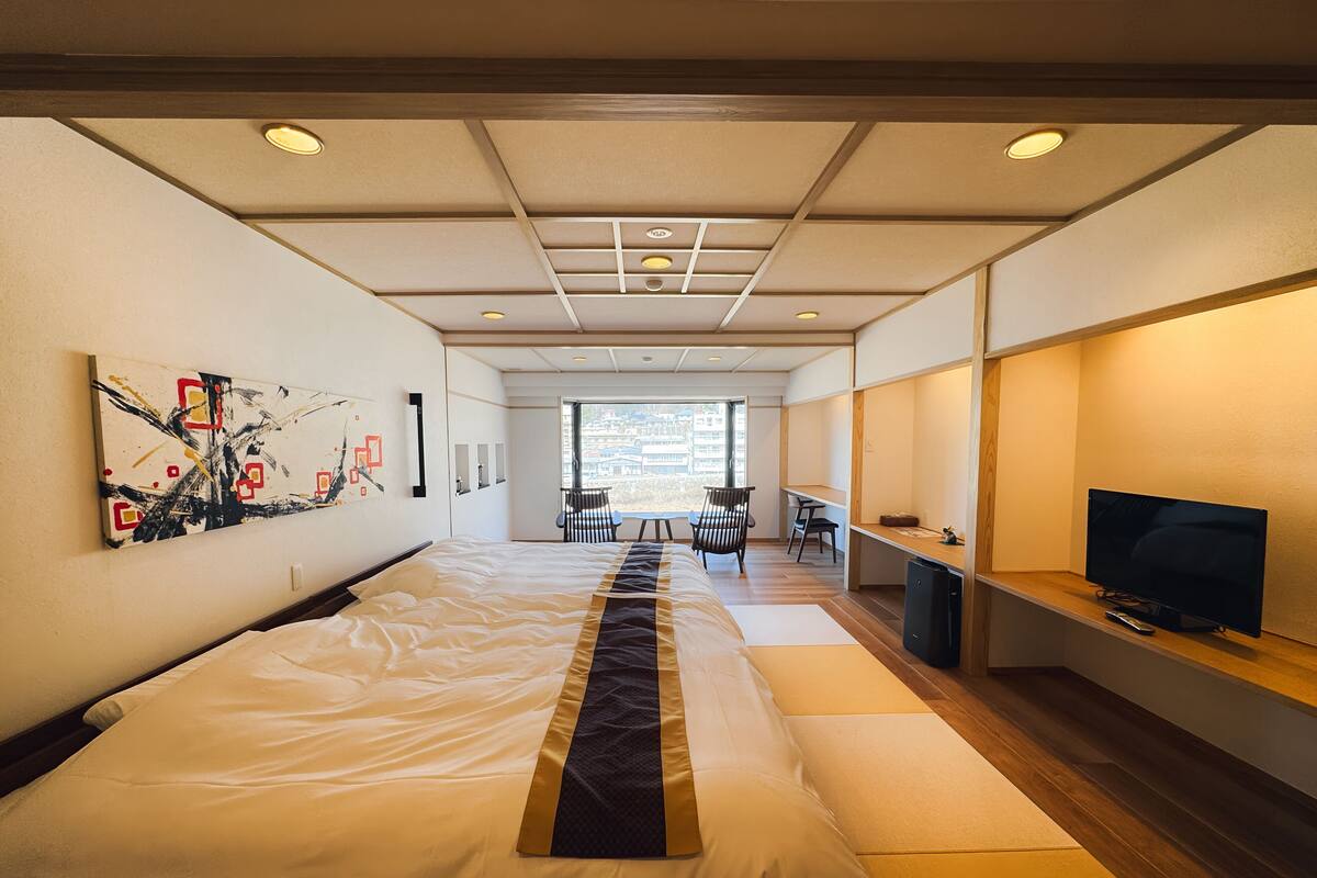 Une chambre d’hôtel moderne dotée d’un grand lit, d’un bureau avec une télévision et offrant une vue sur la ville grâce à de grandes fenêtres.