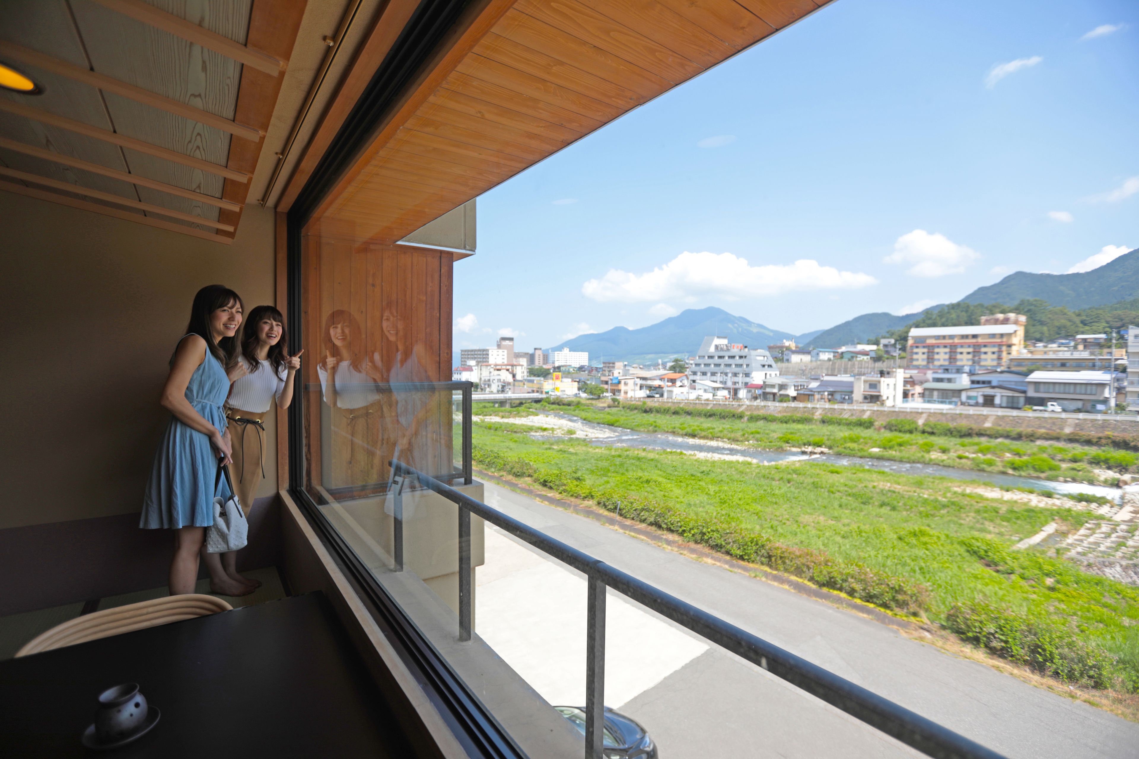 A room with a large window overlooking a river and mountains.