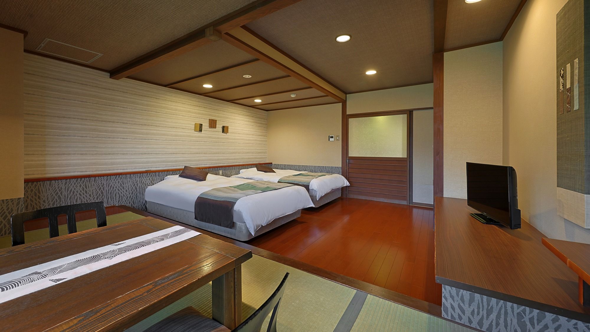 A hotel room with two beds, a wooden dining table, a flat-screen TV, and a sliding door.