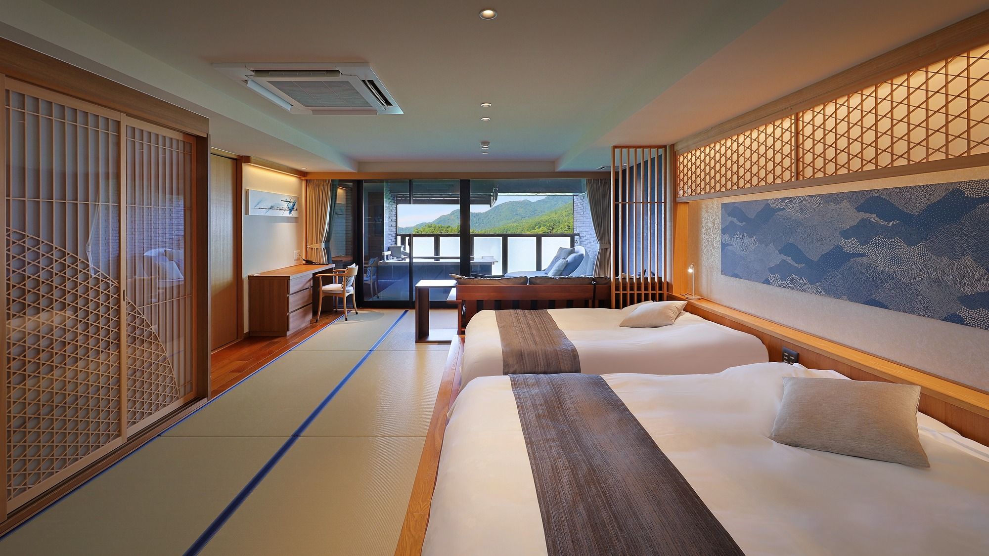 A hotel room with two beds, a desk, and a view of the outdoors.