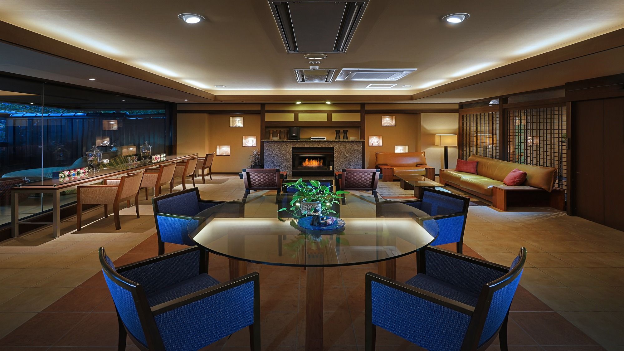 A spacious living room with a glass-top dining table surrounded by chairs, a fireplace, and a seating area with a sofa and armchairs.