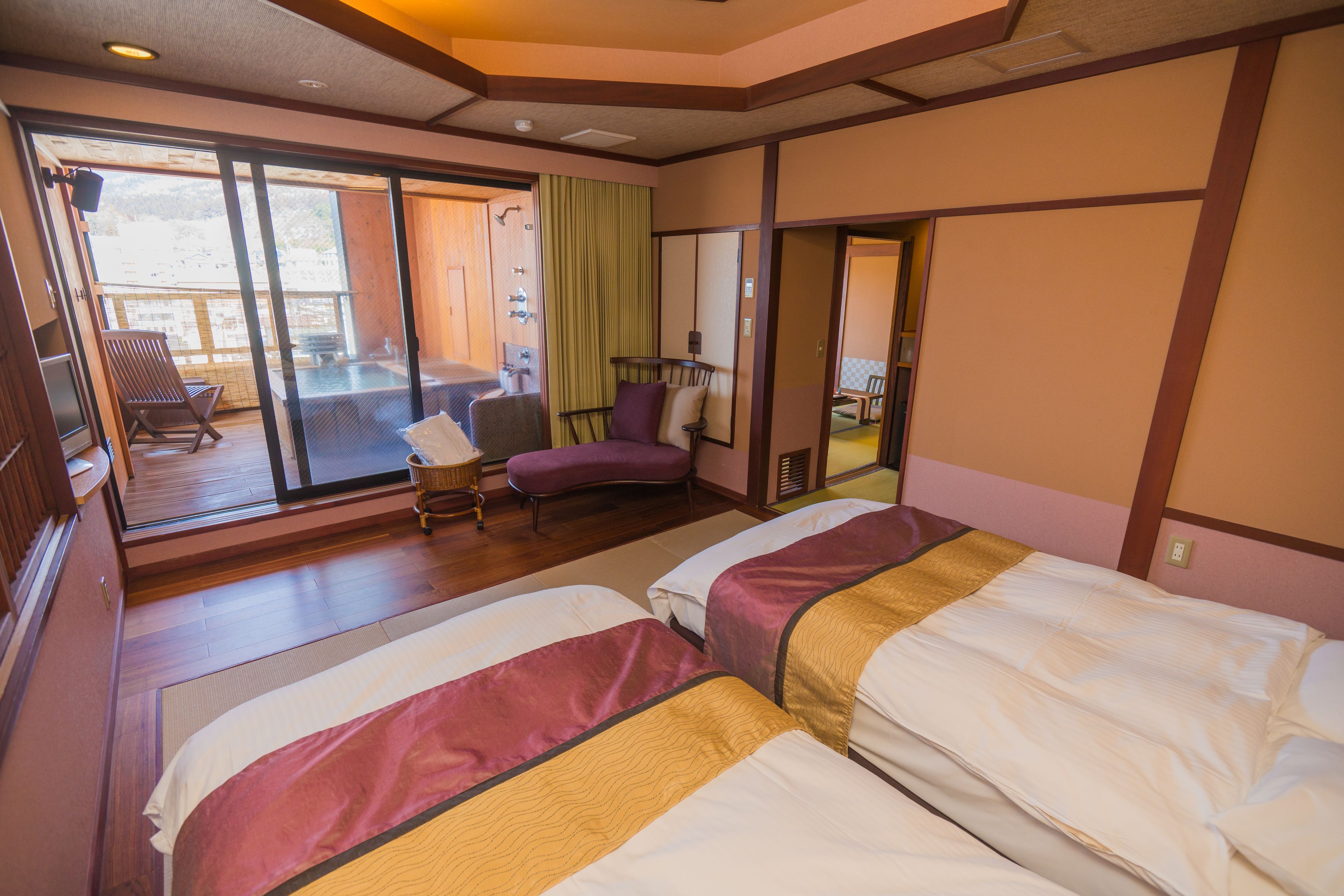 A hotel room with two beds, a balcony, a chair, and a small table.