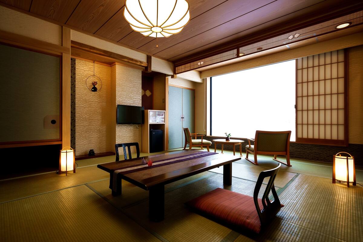 Une pièce de style japonais traditionnel, avec un sol recouvert de tatamis, une table basse, des chaises, un téléviseur et des portes coulissantes.
