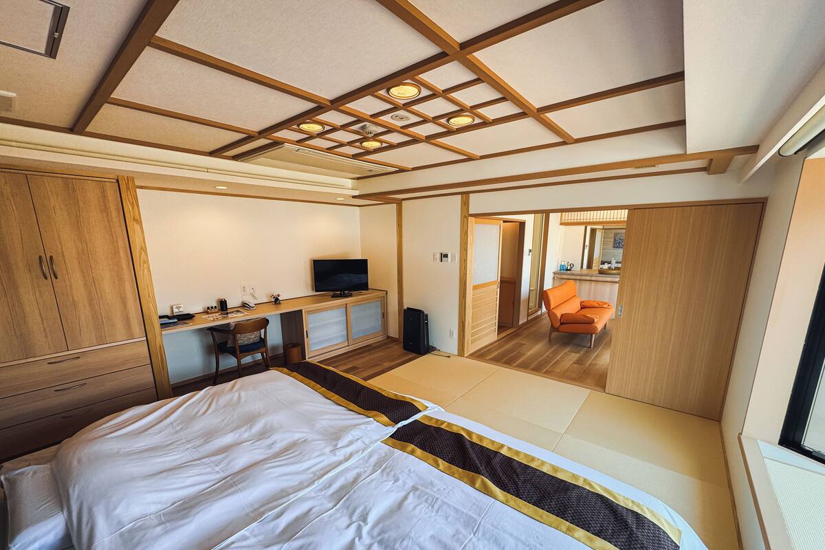 Une chambre d’hôtel comprenant un lit, un bureau avec une télévision, un petit coin cuisine et une salle de bain.