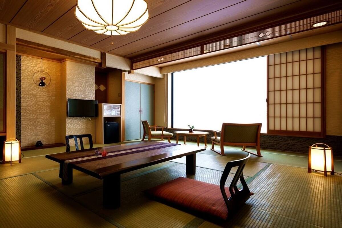 Une pièce de style japonais traditionnel, avec un sol recouvert de tatamis, une table basse, des chaises et des portes coulissantes.