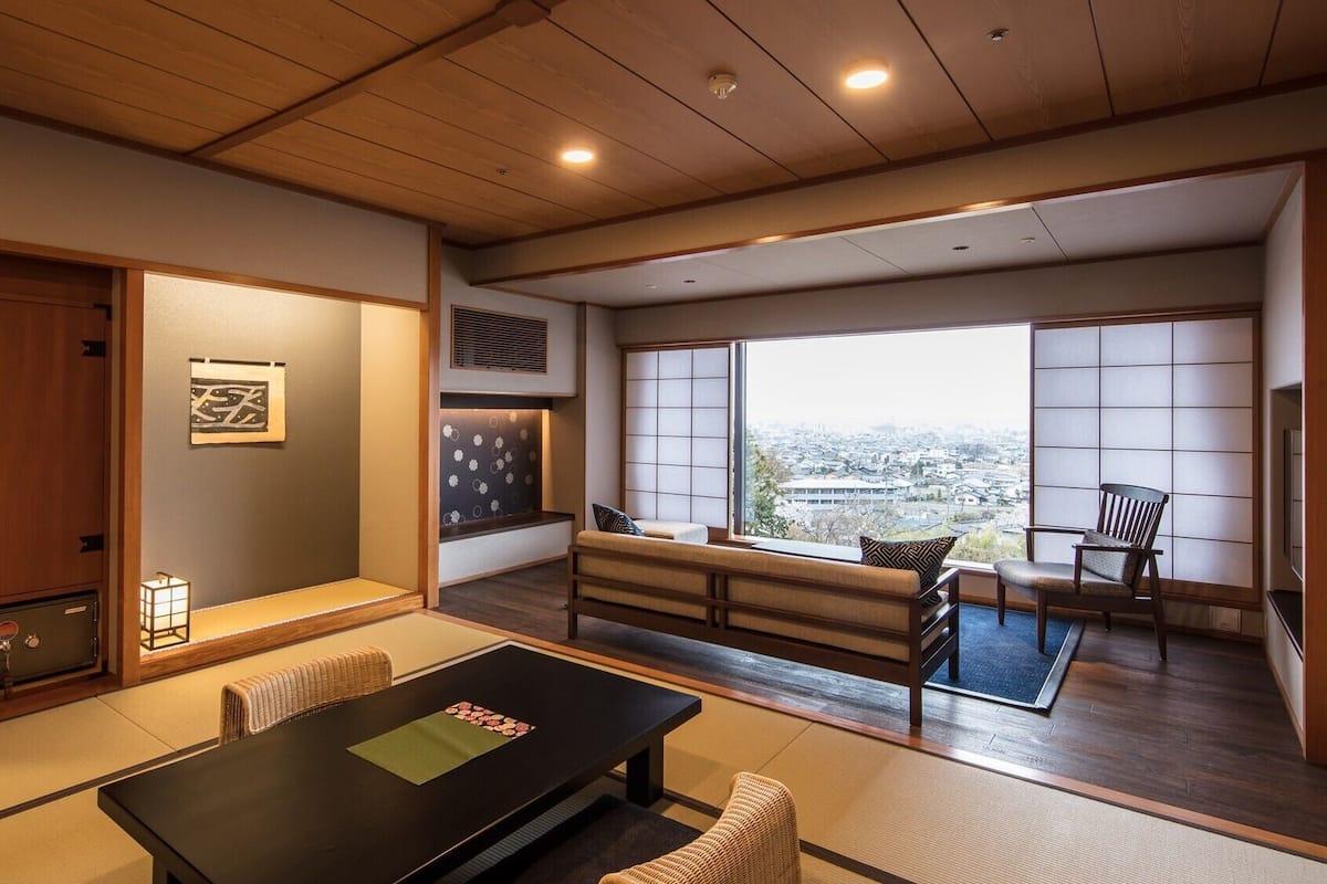 A traditional Japanese room with tatami flooring, a low table, and a view of the city.
