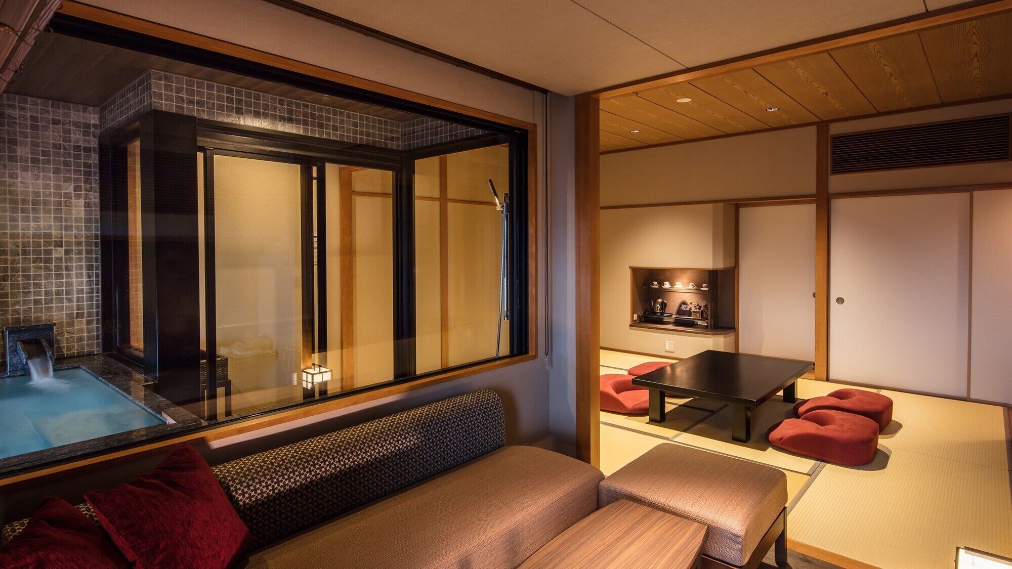A modern interior with a glass-enclosed shower, a seating area with a bench, a table with chairs, and a traditional Japanese-style room with sliding doors.