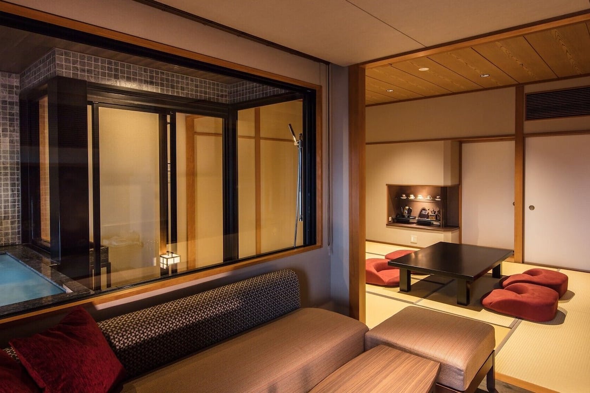 A modern interior with a glass-enclosed shower, a seating area with a bench, a table with chairs, and a traditional Japanese-style room with sliding doors.