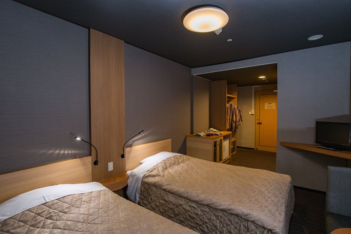 A hotel room with two beds, a desk with a television, and a wardrobe.