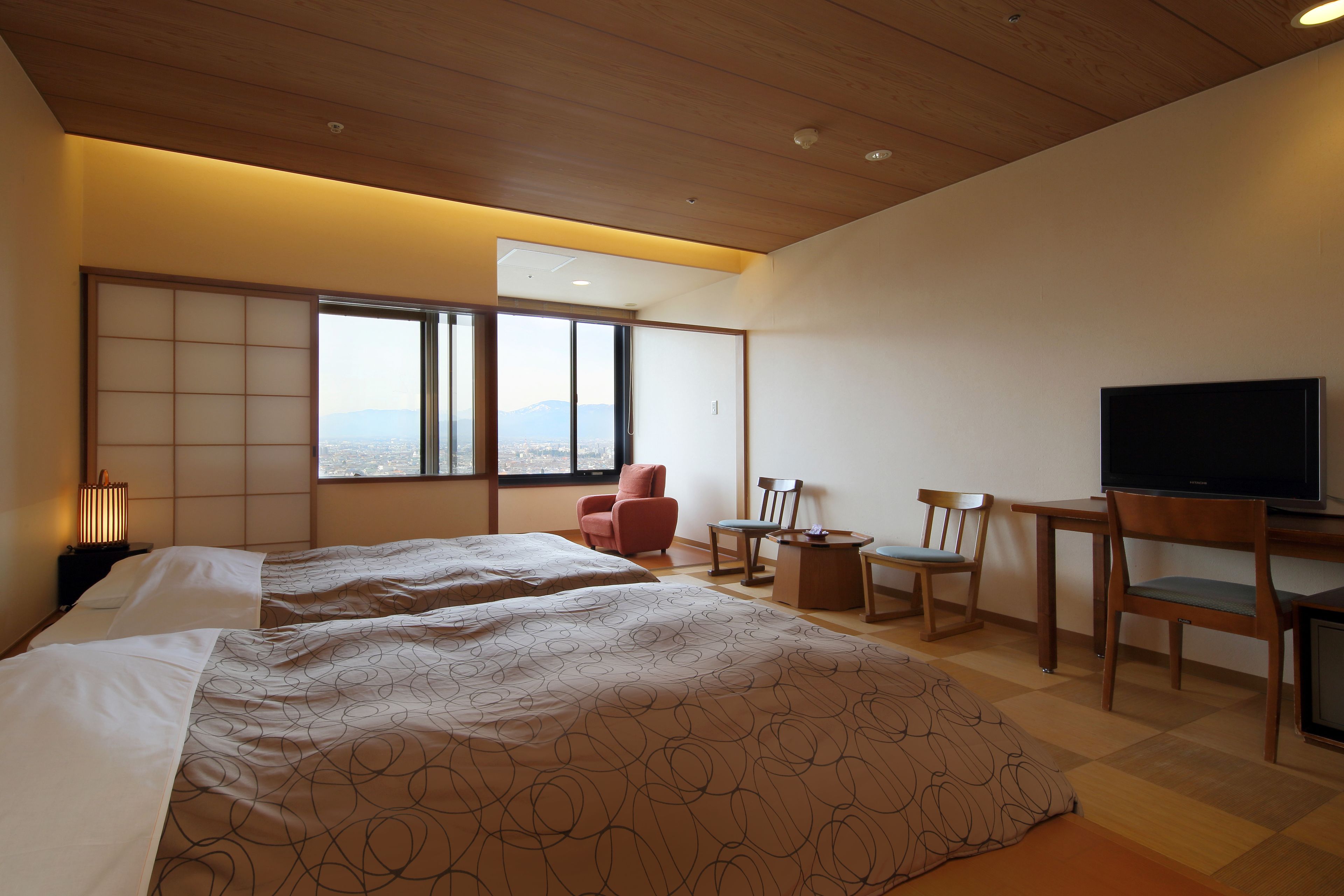A hotel room with two beds, a TV, a desk with chairs, and a view of the city.