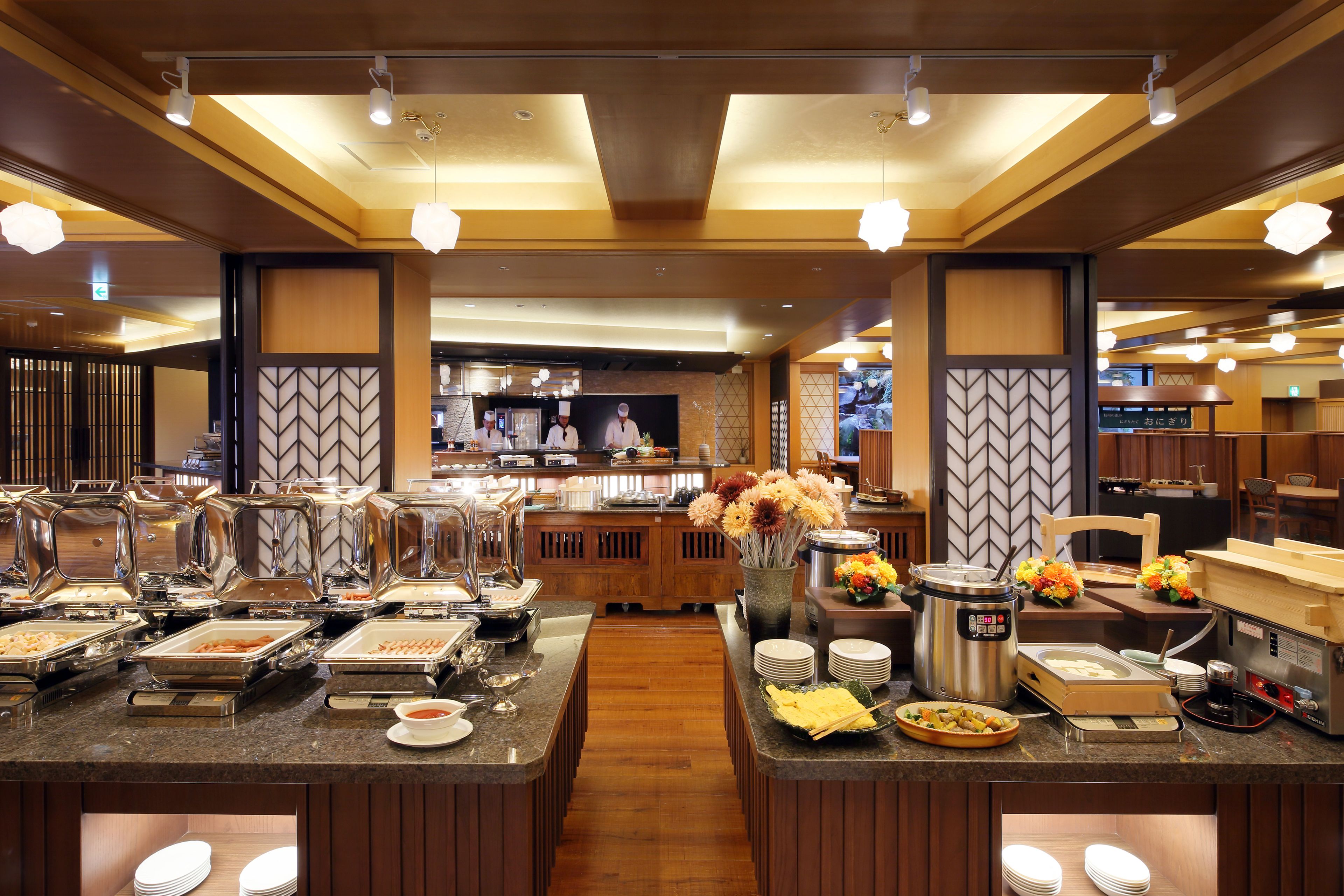A buffet area with various food stations, a coffee machine, and a seating area with a wooden table and chairs.