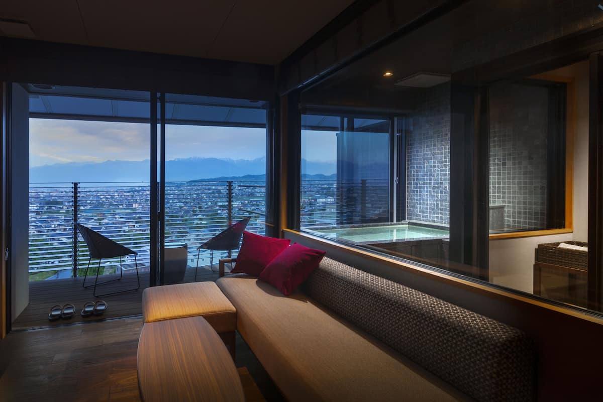 A modern room with a large sliding glass door leading to a balcony with a city view.