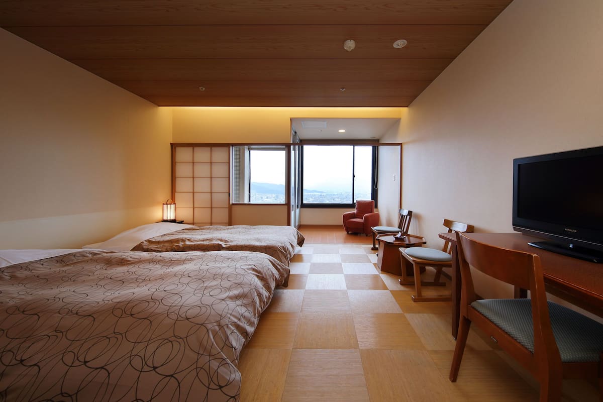 A hotel room with a large bed, a television, a desk, and a view of the city.