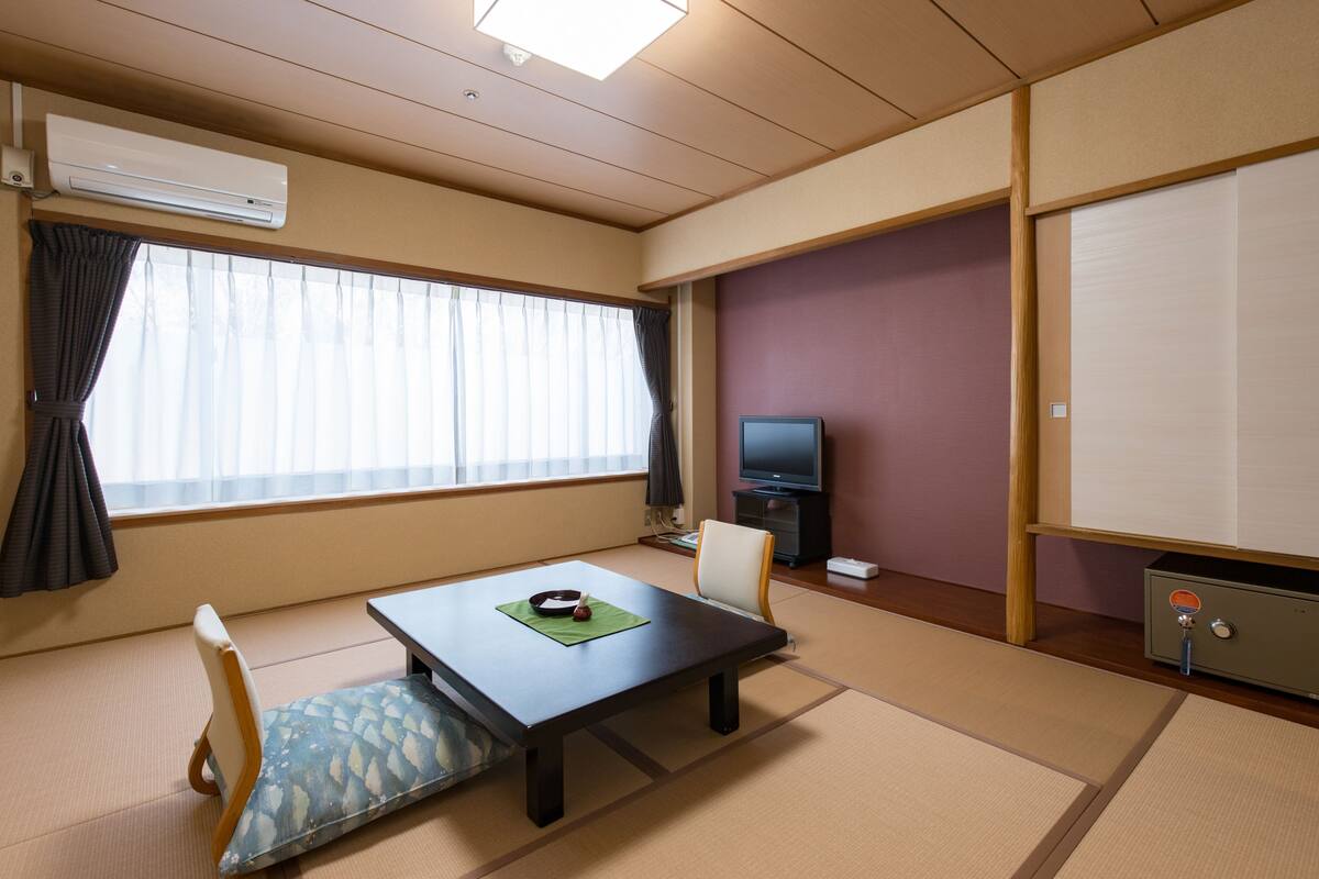 A traditional Japanese room with tatami flooring, a low table with a green placemat, a television, and a sliding door.