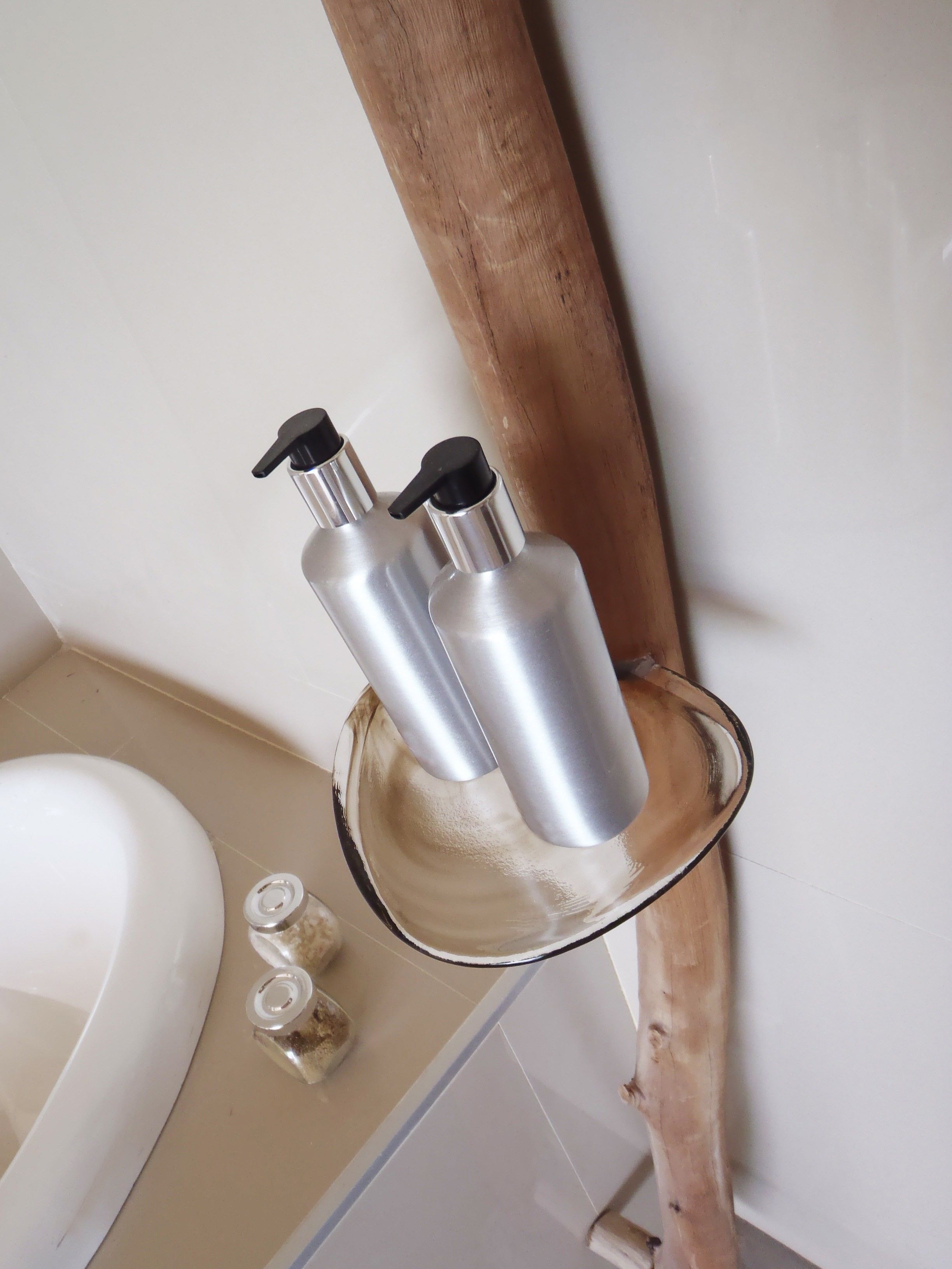 Un baño con una bañera blanca, un estante de madera que sostiene dos botellas metálicas y un inodoro.