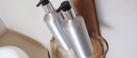 Un baño con una bañera blanca, un estante de madera que sostiene dos botellas metálicas y un inodoro.