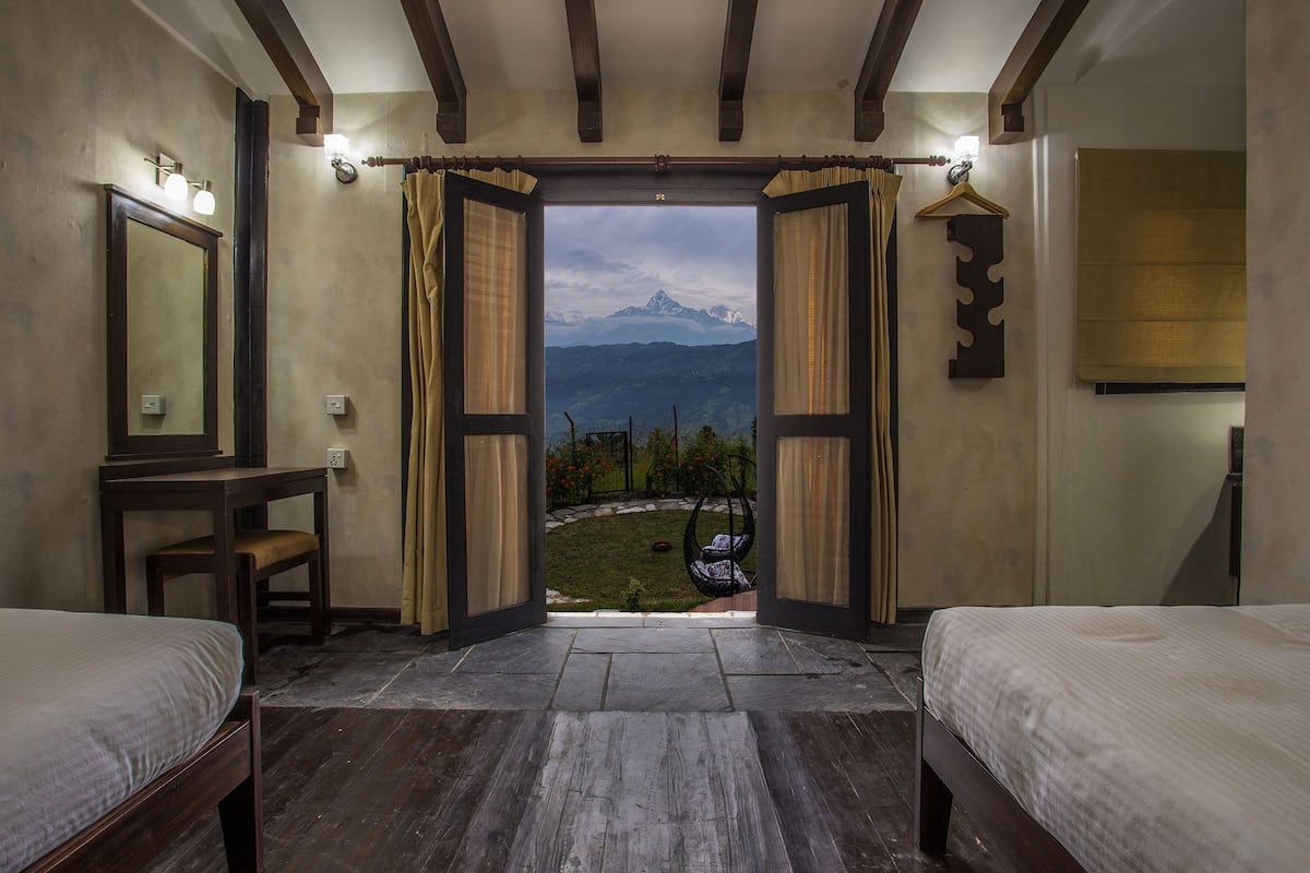 A bedroom with two beds, a wooden floor, a view of mountains, and a hanging chair outside.